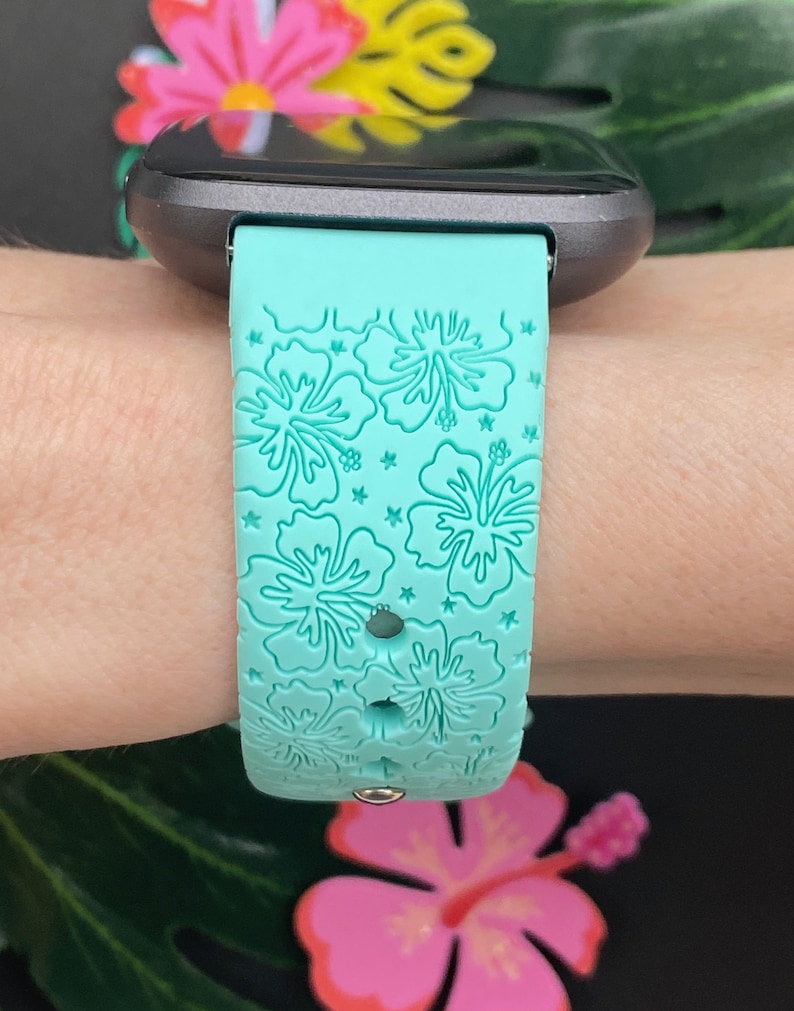 May include: A turquoise silicone watch band with a floral pattern. The band has a white hibiscus flower design.