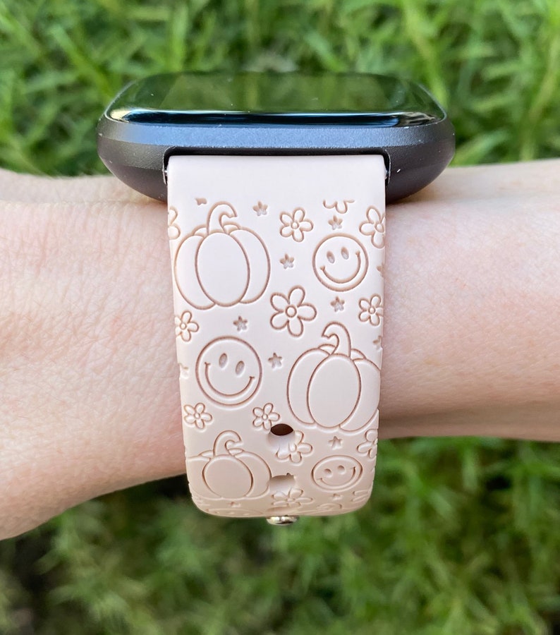 Pu&ograve; includere: Un cinturino per orologio in silicone rosa con un motivo di zucche, faccine sorridenti e fiori. Il cinturino &egrave; progettato per uno smartwatch.