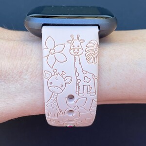 May include: A pink silicone watch band with a giraffe and flower design. The band is compatible with smartwatches.