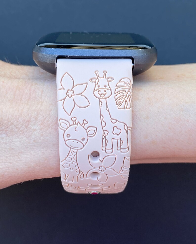 May include: A pink silicone watch band with a giraffe and flower design. The band is compatible with smartwatches.