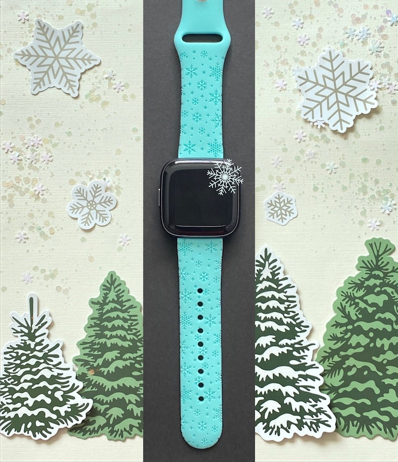 May include: A turquoise blue Apple Watch band with a snowflake pattern. The band is made of silicone and has a smooth finish. The watch band is shown on a white background with snowflakes and Christmas trees.