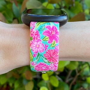 Op de afbeelding: Een zwarte smartwatch met een band met bloemenprint. De band is turquoise met roze, witte en groene bloemen.