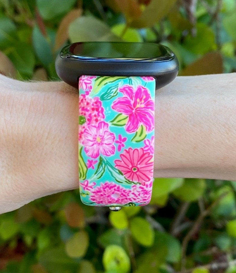 Op de afbeelding: Een zwarte smartwatch met een band met bloemenprint. De band is turquoise met roze, witte en groene bloemen.