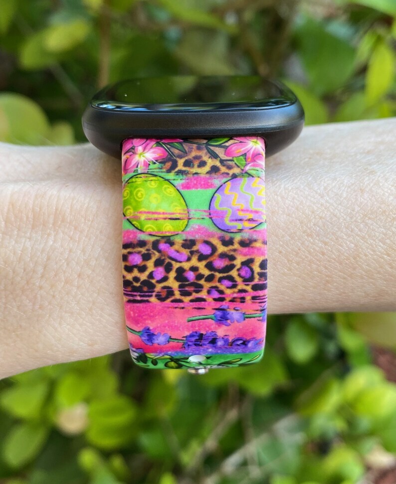 May include: A colorful watch band with a pink, green, and purple Easter egg design. The band has a leopard print pattern and floral accents.
