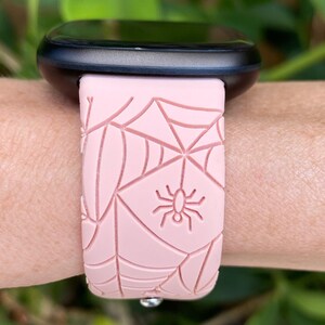 May include: A pink silicone watch band with a spider web and spider design. The band is compatible with smartwatches.