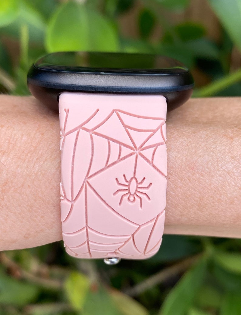 May include: A pink silicone watch band with a spider web and spider design. The band is compatible with smartwatches.