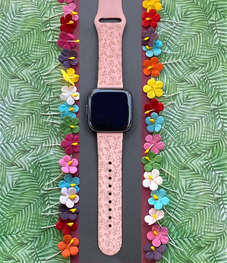 May include: A pink smartwatch band with a floral pattern. The band is made of silicone and has a black watch face.