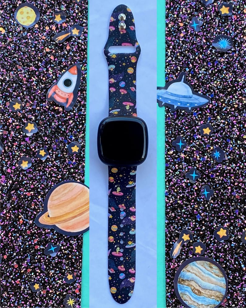 May include: A black watch band with a space-themed pattern featuring planets, stars, rockets, and UFOs. The band is made of silicone and has a black buckle.