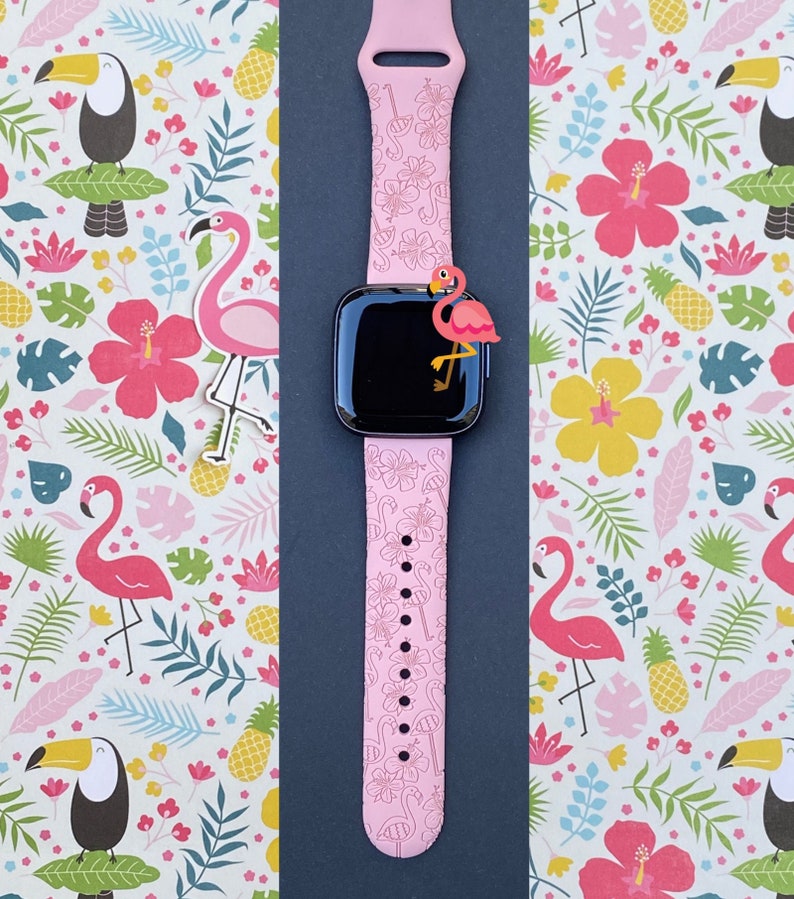 May include: Pink Apple Watch band with a tropical flamingo print. The band is made of silicone and has a black buckle.