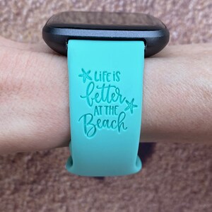 May include: A turquoise blue silicone watch band with the text "Life is better at the beach" and a starfish graphic.
