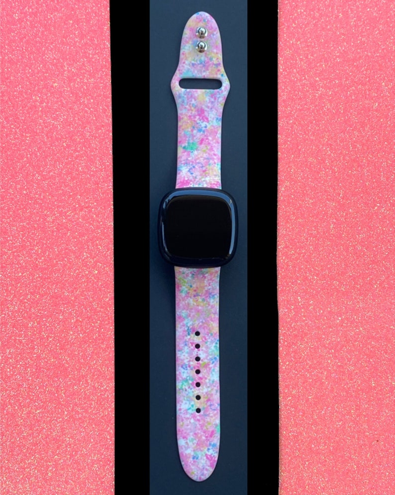 May include: A pink, white, and blue patterned Apple Watch band with a black Apple Watch face.