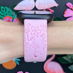 May include: Pink silicone watch band with a flamingo and floral pattern. The band is designed for a smartwatch.