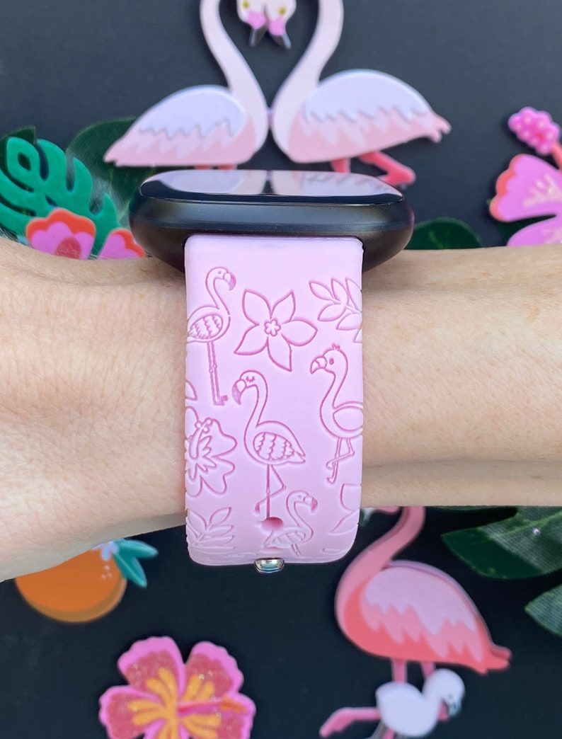 May include: Pink silicone watch band with a flamingo and floral pattern. The band is designed for a smartwatch.