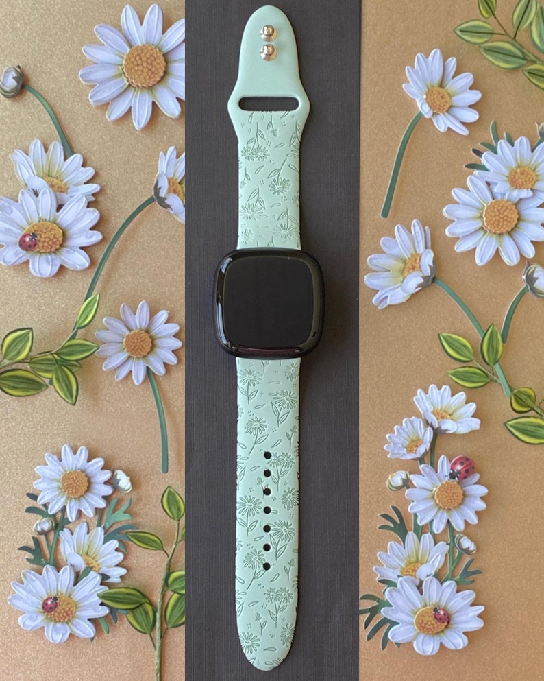 May include: A light green watch band with a floral pattern. The band is made of silicone and has a black watch face.