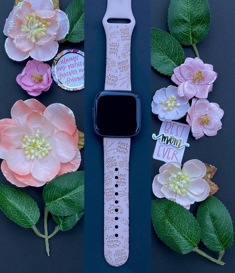 May include: A pink Apple Watch band with a floral design and gold lettering. The band has the words "best mom ever", "love you mom", "always my mother forever my friend", and "cherished always you're the best mom ever" printed on it.