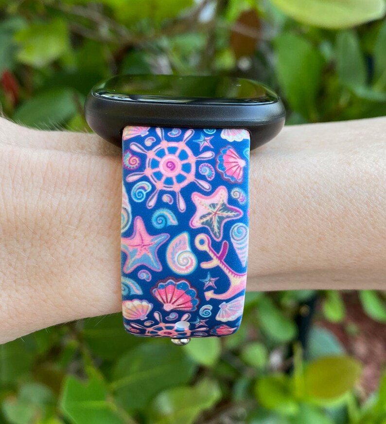 K&ouml;nnte beinhalten: Ein blaues und pinkfarbenes Armband mit nautischem Muster. Das Armband zeigt Muscheln, Anker und Seesterne.