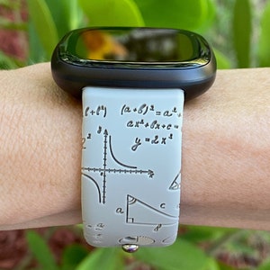 May include: A white smartwatch band with a black watch face. The band has a pattern of mathematical equations and symbols, including a graph, a triangle, and the equation "y=2x^2".