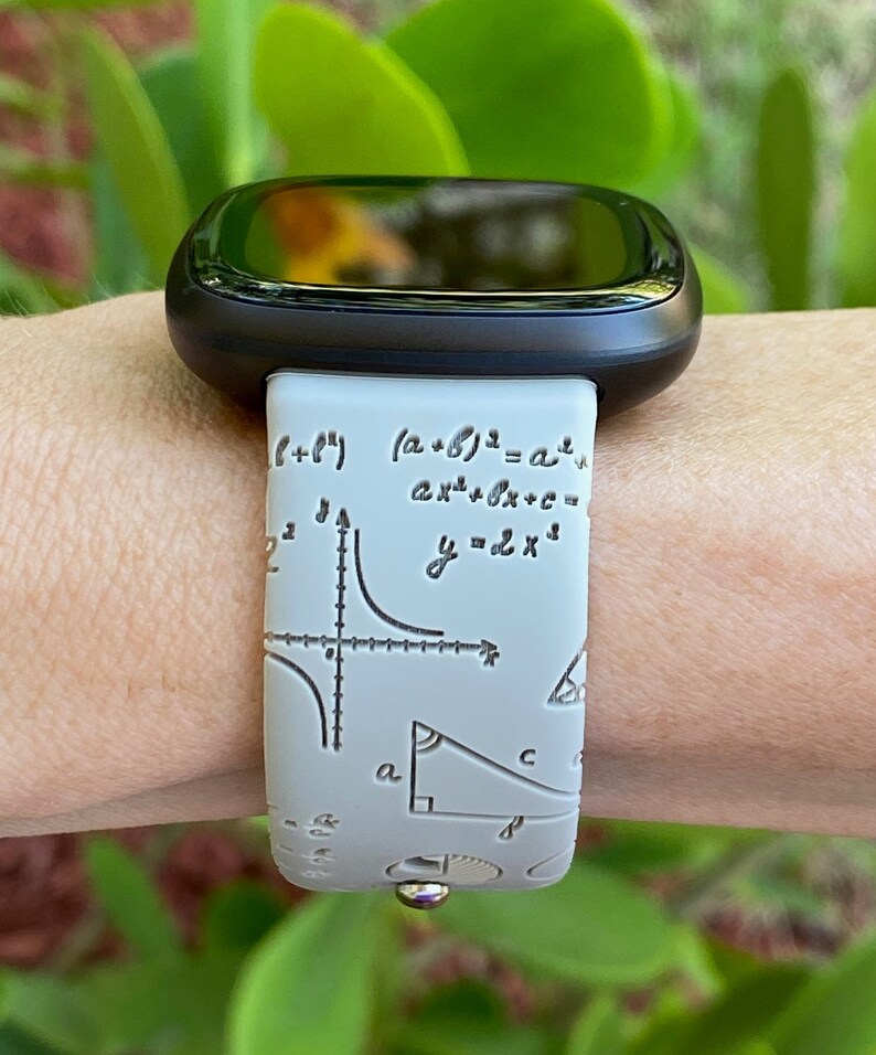 May include: A white smartwatch band with a black watch face. The band has a pattern of mathematical equations and symbols, including a graph, a triangle, and the equation "y=2x^2".