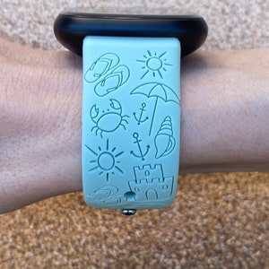 May include: A light blue watch band with a variety of summer-themed illustrations, including flip flops, a sun, an umbrella, a crab, an anchor, a seashell, and a sandcastle.