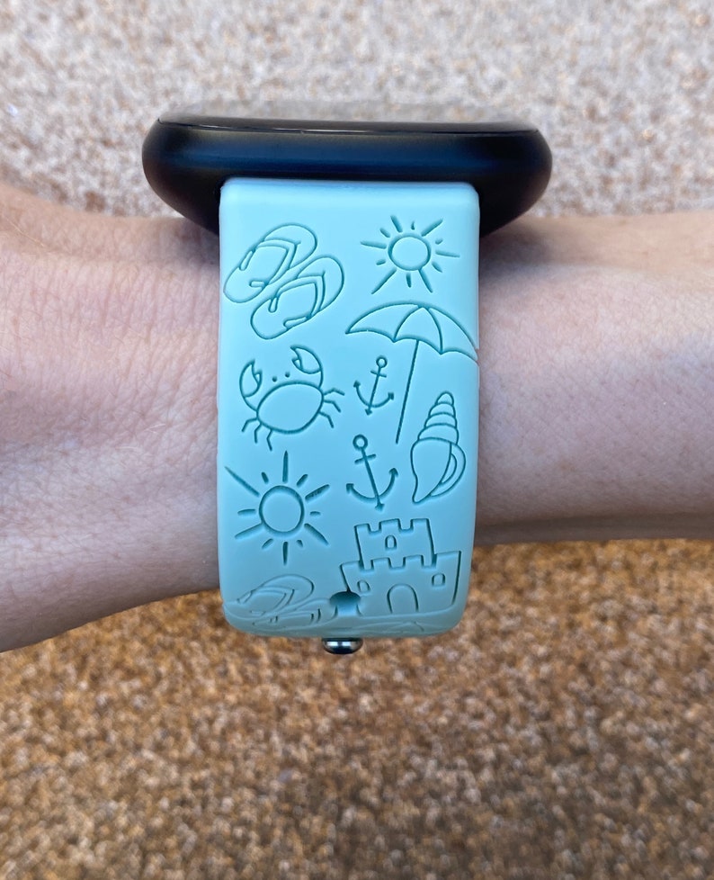 May include: A light blue watch band with a variety of summer-themed illustrations, including flip flops, a sun, an umbrella, a crab, an anchor, a seashell, and a sandcastle.