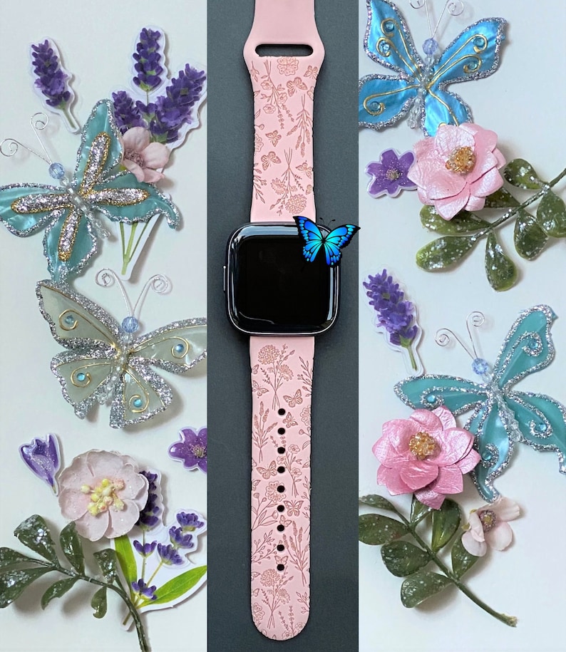 May include: A pink Apple Watch band with a floral design. The band is decorated with small butterflies and flowers. The watch face is black and shows the time.