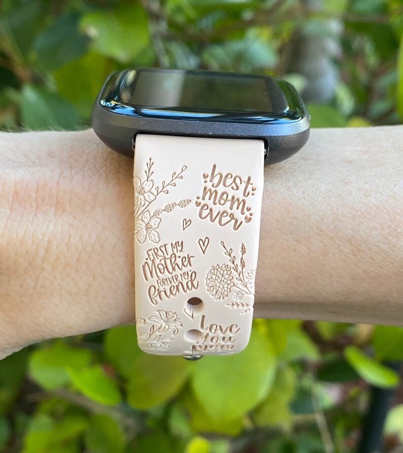 May include: A beige smartwatch band with a floral design and the text "best mom ever", "first my mother forever my friend", and "love you".