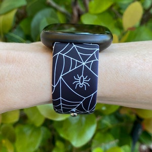 May include: A black and white watch band with a spider web and spider design.