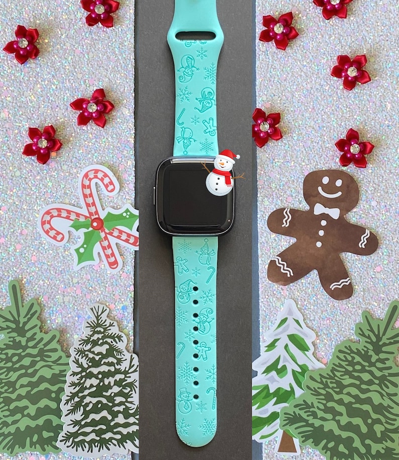 May include: A turquoise blue smartwatch band with a Christmas theme. The band features snowflakes, candy canes, gingerbread men, and snowmen.