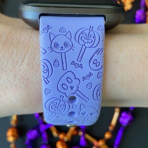 May include: A lavender silicone watch band with a Halloween theme. The band features a repeating pattern of pumpkins, bats, candy corn, and ghosts.