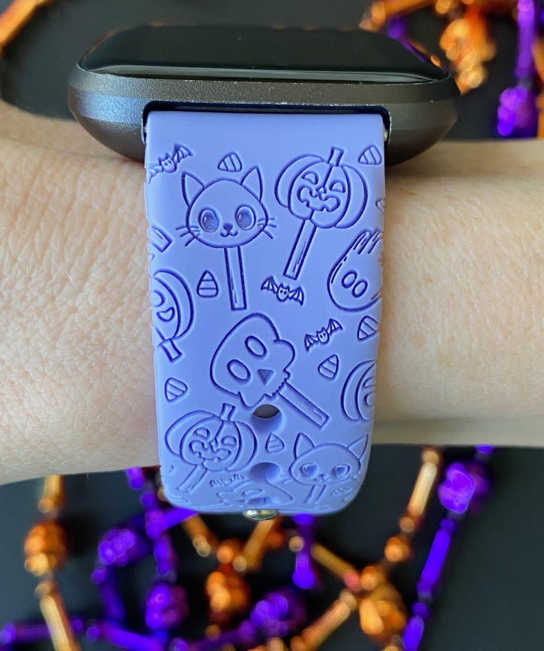 May include: A lavender silicone watch band with a Halloween theme. The band features a repeating pattern of pumpkins, bats, candy corn, and ghosts.
