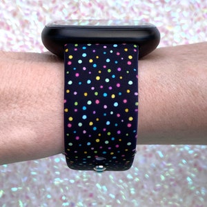 May include: A black smartwatch with a colorful polka dot patterned band. The band has small, multi-colored dots on a black background.