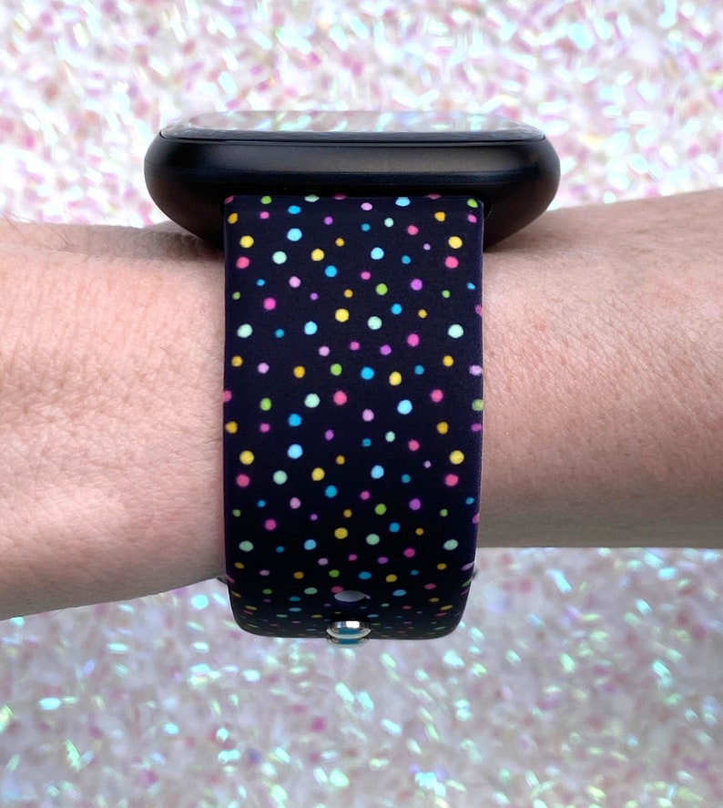 May include: A black smartwatch with a colorful polka dot patterned band. The band has small, multi-colored dots on a black background.