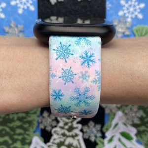 May include: A white Apple Watch band with a snowflake pattern in blue and pink. The band is made of silicone and has a glittery finish.