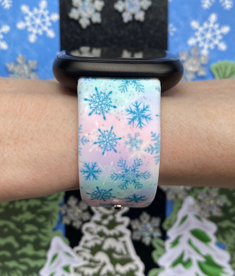 May include: A white Apple Watch band with a snowflake pattern in blue and pink. The band is made of silicone and has a glittery finish.