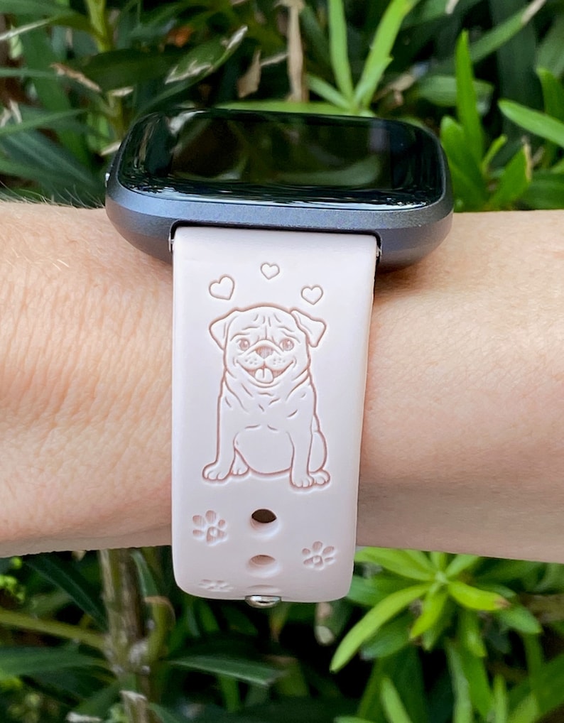 May include: A pink silicone watch band with a white pug design and three hearts. The band has a silver buckle and is compatible with a smartwatch.
