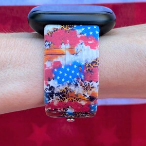 Pu&ograve; includere: Uno smartwatch nero con un cinturino colorato che presenta un design di bandiera americana rosso, bianco e blu con accenti leopardati.