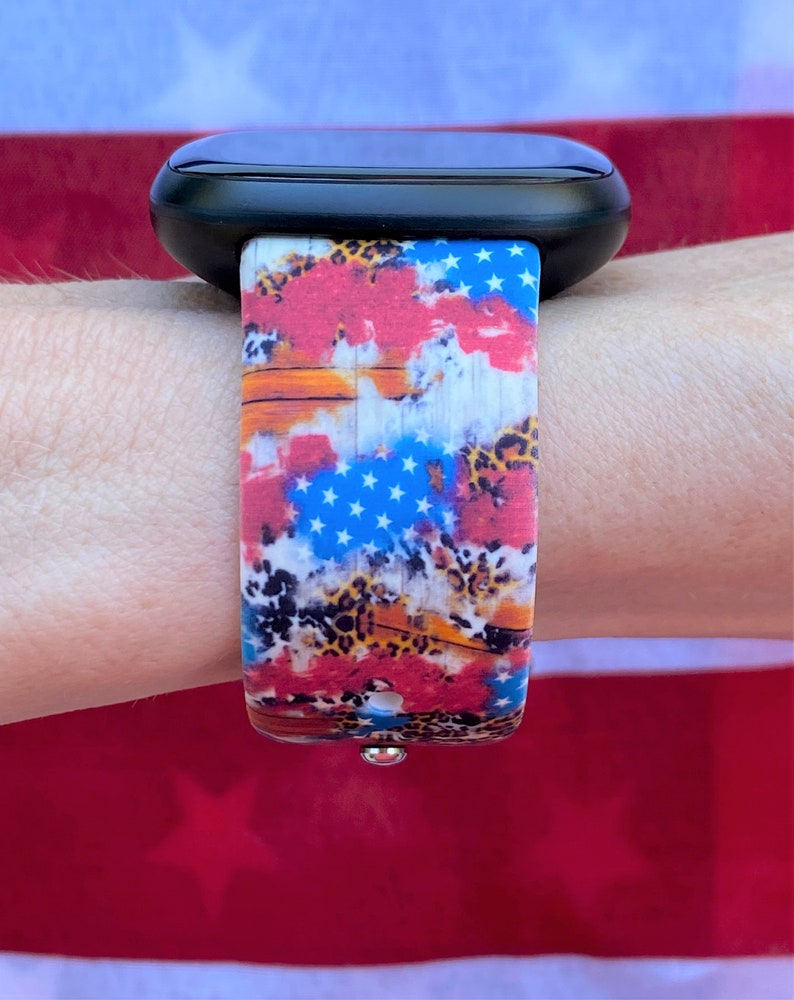 Pu&ograve; includere: Uno smartwatch nero con un cinturino colorato che presenta un design di bandiera americana rosso, bianco e blu con accenti leopardati.