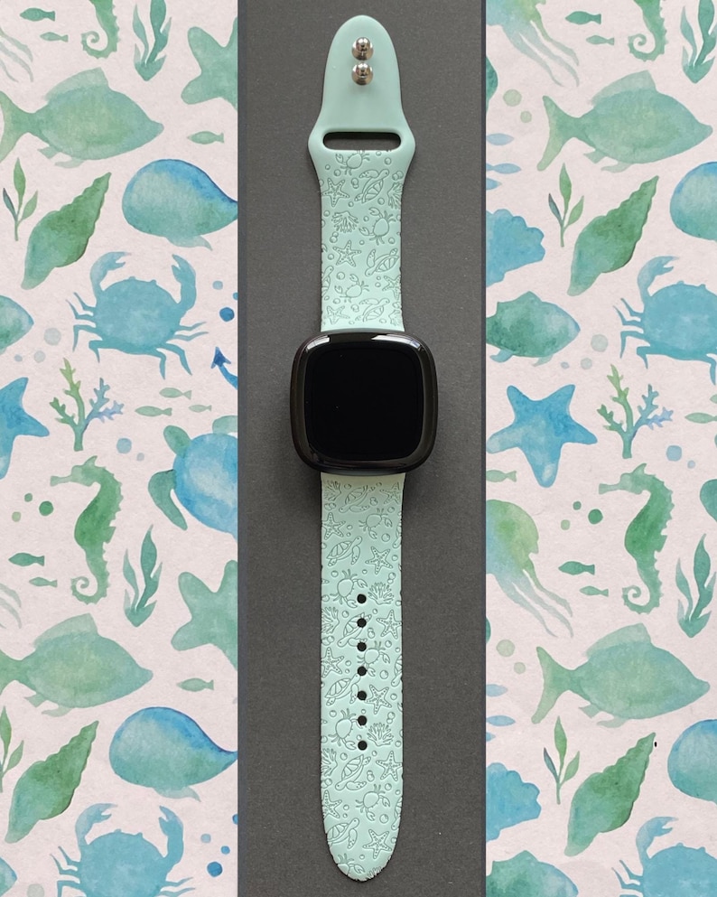 May include: A light blue silicone watch band with a sea life pattern. The band has a white background with embossed images of seahorses, fish, seashells, and starfish. The band is compatible with smartwatches.