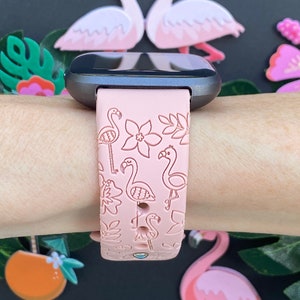 May include: A pink silicone watch band with a flamingo and floral pattern. The band is designed for a smartwatch and has a black watch face.