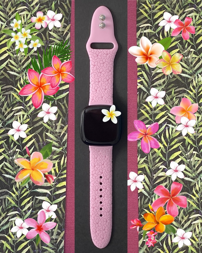 May include: A pink silicone watch band with a black watch face. The band has a floral pattern and the watch face has a black background.