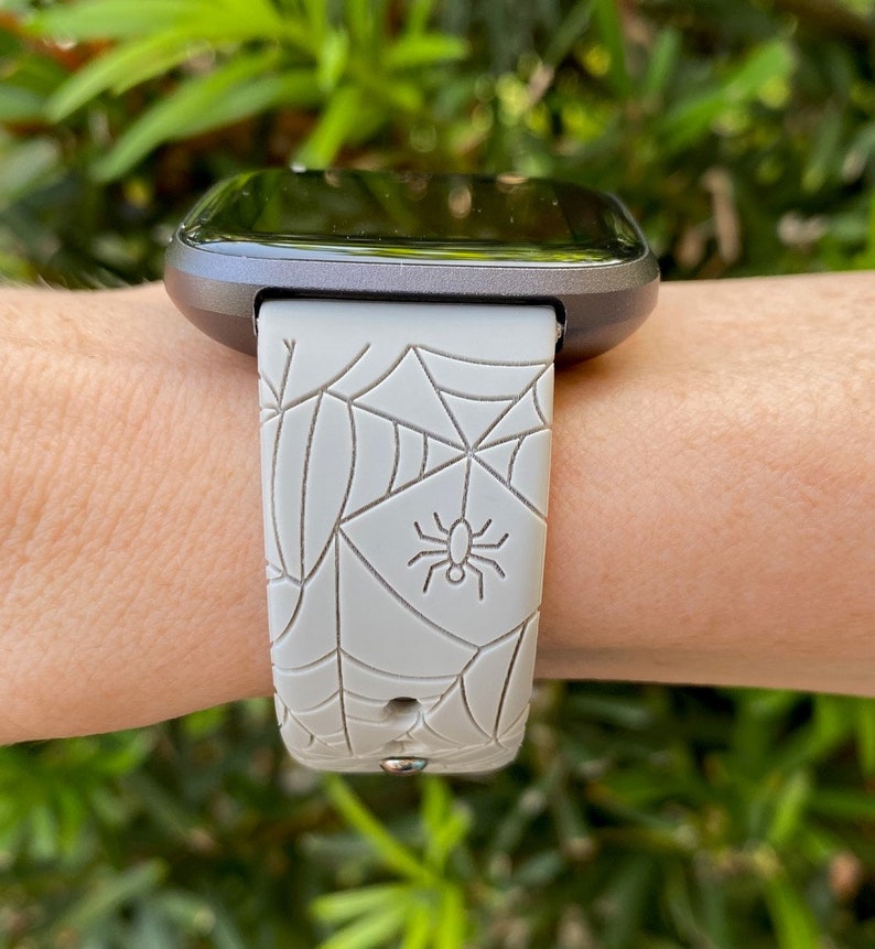 May include: A gray smartwatch with a spiderweb and spider design on the band.