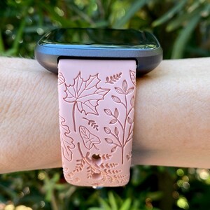 May include: A pink fitness tracker band with a floral pattern. The band has a detailed design of leaves and flowers.