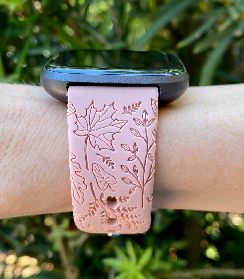 May include: A pink fitness tracker band with a floral pattern. The band has a detailed design of leaves and flowers.