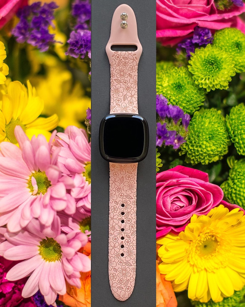 May include: A pink smartwatch with a floral pattern band. The watch face is black and the band has a delicate floral design.
