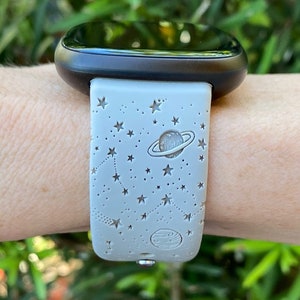 May include: A gray smartwatch band with a white background and a design of stars and planets. The band is made of silicone and has a smooth finish.