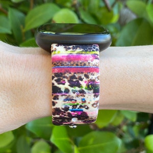 May include: A black fitness tracker with a colorful leopard print band. The band has stripes of pink, yellow, green, and blue.