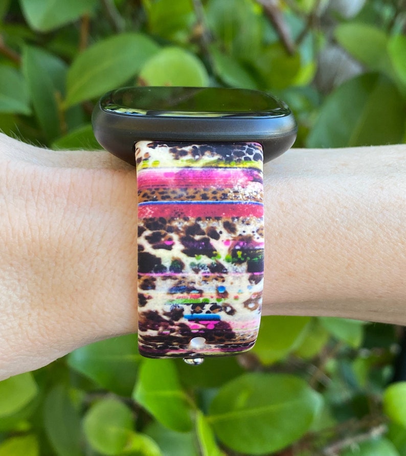 May include: A black fitness tracker with a colorful leopard print band. The band has stripes of pink, yellow, green, and blue.
