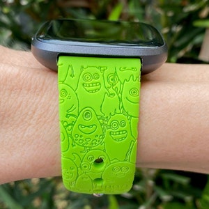 Puede incluir: Una banda de reloj inteligente verde con un dise&ntilde;o de monstruo de dibujos animados. La banda est&aacute; hecha de silicona y tiene una hebilla negra.