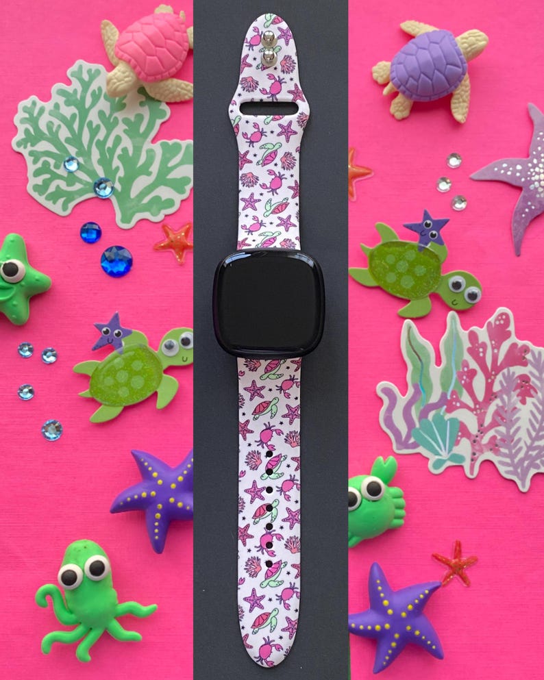 Puede incluir: Correa blanca para smartwatch con un estampado de vida marina rosa y verde, que incluye cangrejos, estrellas de mar y tortugas. La esfera del reloj es negra. La correa est&aacute; rodeada de criaturas marinas decorativas y coral sobre un fondo rosa brillante.