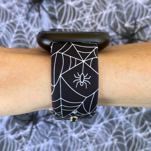 May include: Black and white watch band with a spider web and spider design.